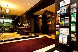 Eine Hotelhalle mit Empfangsbereich, Sitzgelegenheiten und einer Broschürenauslage.