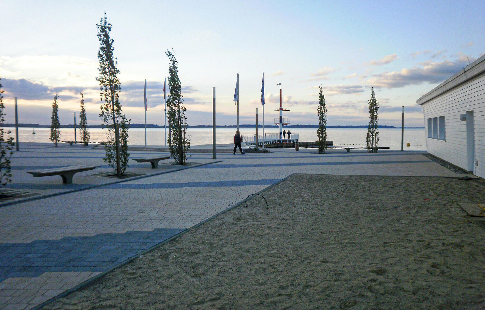 Une promenade en bord de mer, agrémentée de bancs, d’un petit bâtiment et de drapeaux.