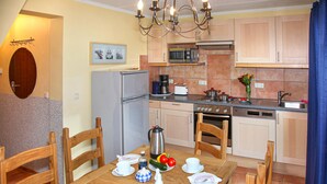 A compact kitchen with a refrigerator, stove, microwave, and sink. There is a dining table with chairs and a chandelier.