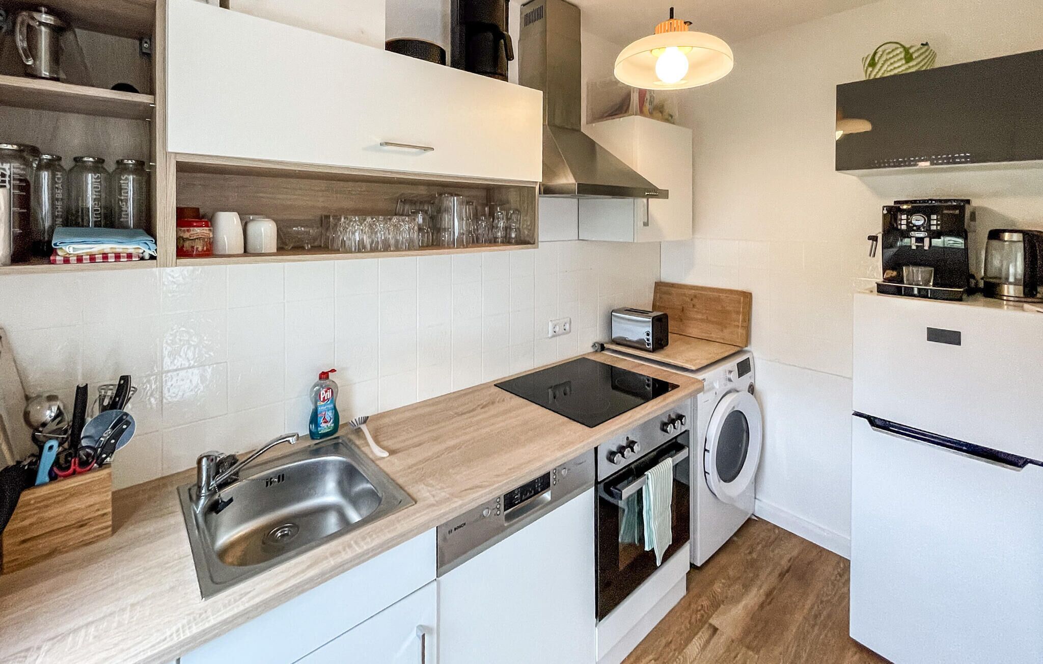 A compact kitchen with a sink, stove, and dishwasher, wooden countertops, and a coffee machine.