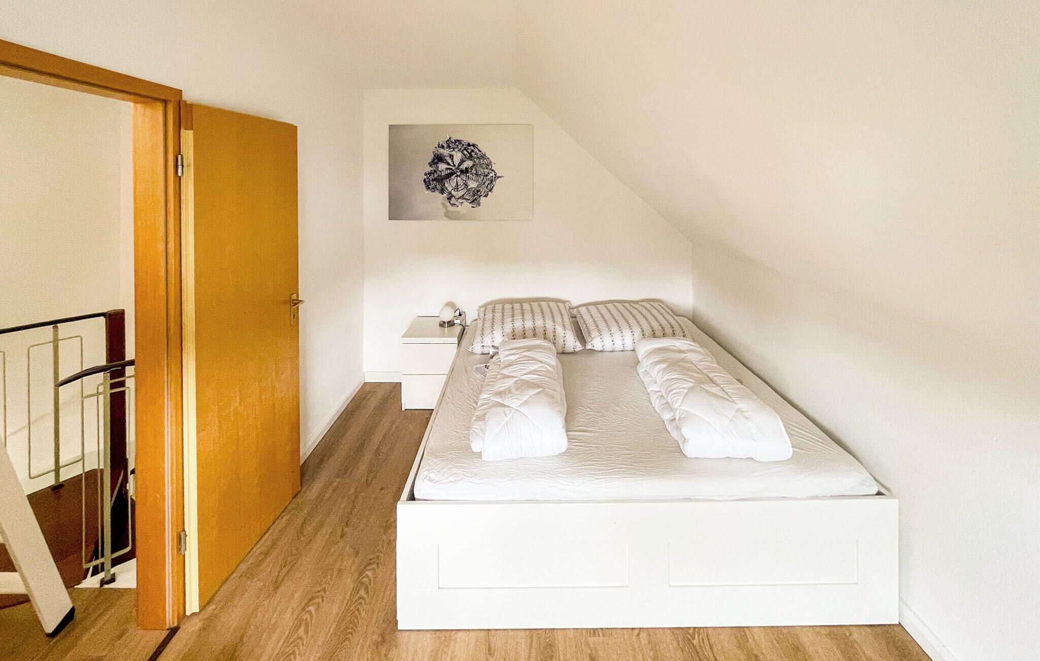 A small, neatly arranged bedroom with a bed, bedside table, and a wall-mounted artwork.