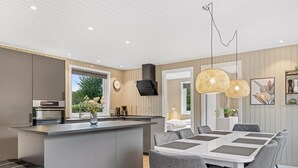 A modern kitchen with a central island, a dining area with a white table and grey chairs, and a living space with a bed and a TV. - "Lymke" - 450m from the sea by Interhome (Sydals)