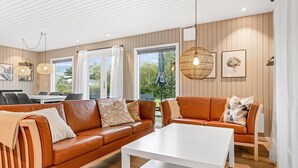 A modern living room with a brown leather sofa, white coffee table, and a dining area with a table and chairs. - "Lymke" - 450m from the sea by Interhome (Sydals)