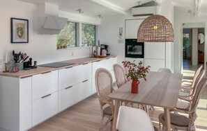 Una cucina moderna con mobili bianchi, un piano di lavoro in legno e un'area pranzo con sedie in vimini e un tavolo.