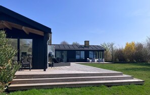 Una casa moderna con terraza, puerta de cristal y mobiliario exterior.