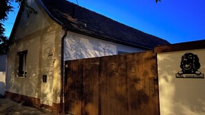 A white building with a dark roof, a wooden fence, and a sign with a dog logo. - Luna Vendégház (Székesfehérvár)