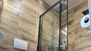 A modern bathroom with a glass-enclosed shower, a white pedestal sink, and wooden wall panels. - Luna Vendégház (Székesfehérvár)
