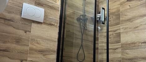 A modern bathroom with a glass-enclosed shower, a white pedestal sink, and wooden wall panels.