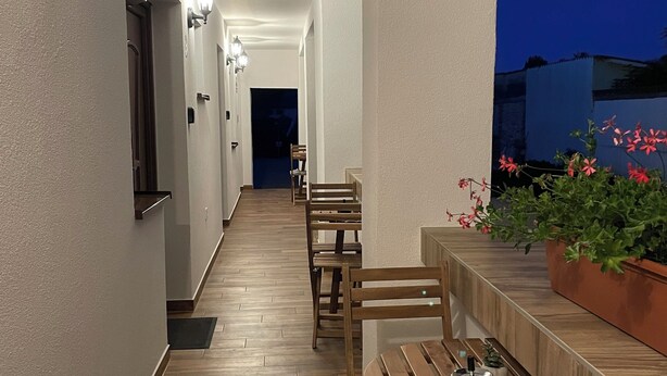 A corridor with wooden benches and a potted plant. - Luna Vendégház (Székesfehérvár)