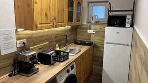 A compact kitchen with wooden cabinets, a built-in washing machine, a microwave, and a coffee maker. - Luna Vendégház (Székesfehérvár)
