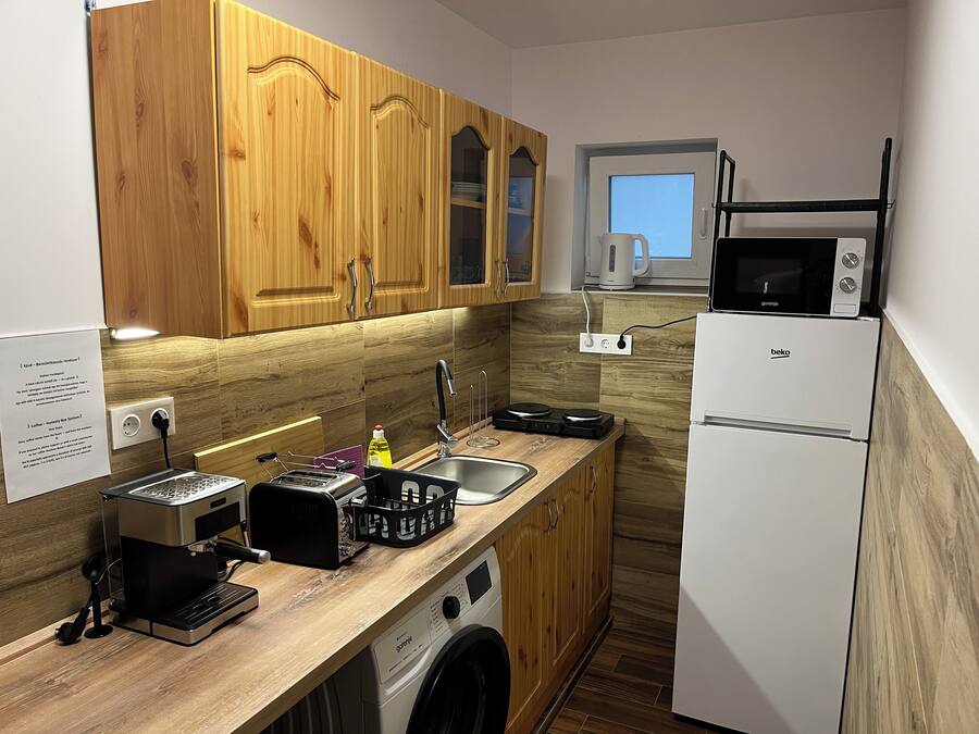 A compact kitchen with wooden cabinets, a built-in washing machine, a microwave, and a coffee maker.