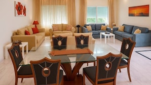 A modern living room with a glass coffee table, two sofas, and a dining area with chairs. - Central Family Apartment  (Amman)