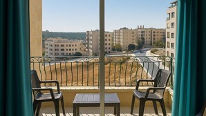 A balcony with two chairs and a table, offering a view of buildings and a road. - Central Family Apartment  (Amman)