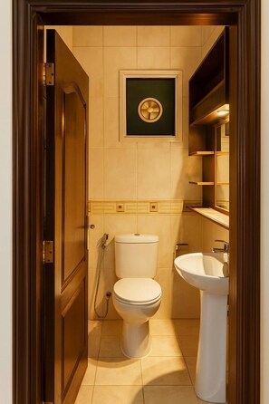Un baño pequeño con inodoro, lavamanos y una pequeña estantería sobre el lavamanos.