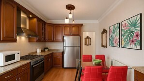 A modern kitchen with wooden cabinets, stainless steel appliances, a glass dining table with red chairs, and tropical-themed wall art. - Central Family Apartment  (Amman)
