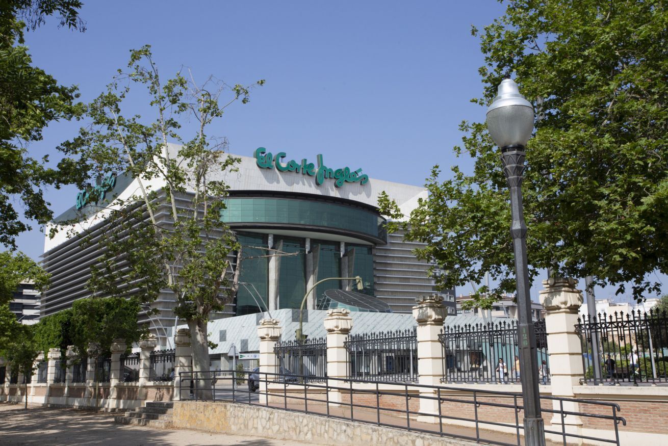 A modern building with a curved facade, a prominent sign reading 'Corte Inglesa,' and a surrounding fence with decorative pillars.