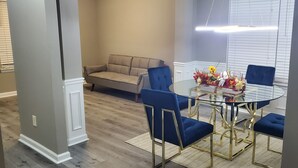 Un comedor con una mesa de vidrio y sillas tapizadas en azul, un sofá beige y un arreglo floral decorativo.