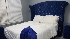 Un dormitorio con una cama azul, ropa de cama blanca y una lámpara decorativa en el techo.