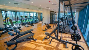 Une salle de sport moderne équipée de divers appareils d’exercice, dotée de grandes fenêtres et d’un plancher en bois.