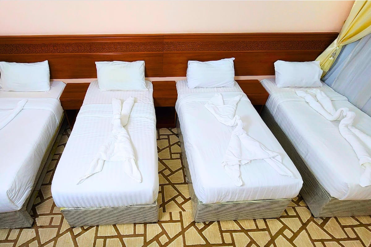 A hotel room with four single beds arranged in a row, each with neatly folded towels and white linens.