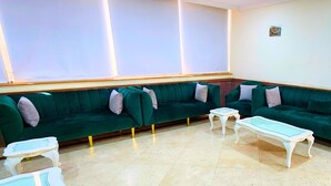A seating area with two green sofas and two white tables, a tiled floor, and a small picture on the wall. - vivyan al Gemmayzeh  (Makkah)
