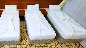 Three single beds with white linens and towels, arranged in a row with a patterned floor and wooden headboard. - vivyan al Gemmayzeh  (Makkah)