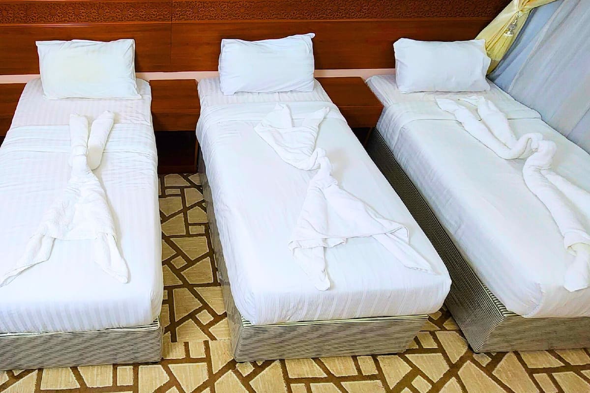 Three single beds with white linens and towels, arranged in a row with a patterned floor and wooden headboard.