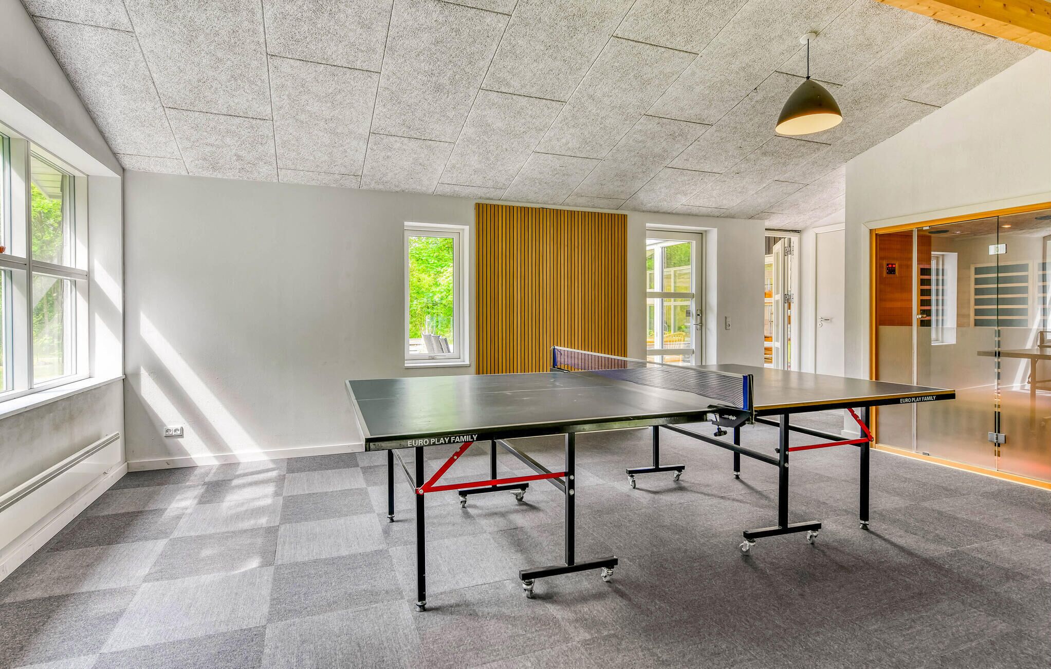 En rummelig stue med et ping pong-bord, store vinduer og et loft med en struktureret overflade.