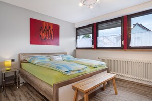 A bedroom with a bed, bedside table, bench, radiator, window, and artwork.