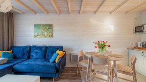 A cozy living room with a blue sofa, a dining table with chairs, and a kitchen area with a microwave.