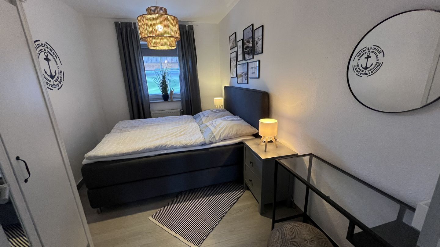 A bedroom with a bed, bedside table, lamp, and a view of the outside through a window.
