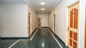 A hallway with a marble floor, white walls, and wooden doors. - Hotel Sun-Om (Raipur)