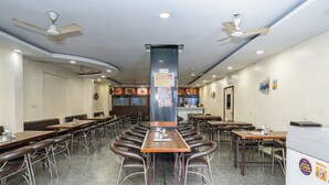 A spacious restaurant with multiple tables and booths, ceiling fans, and a central pillar with a menu board. - Hotel Sun-Om (Raipur)