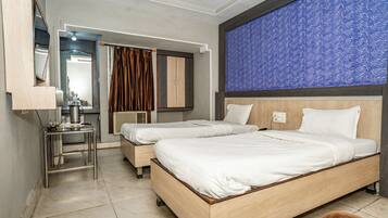 A hotel room with two beds, a small table, a mirror, and a blue patterned wall.