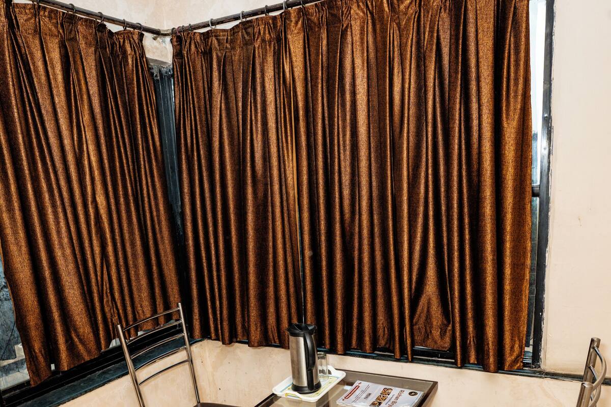 A corner room with a table, chairs, a window with curtains, and a view outside.