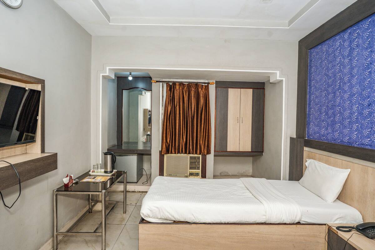 A hotel room with a bed, a desk with a telephone, a mirror, and a wardrobe.