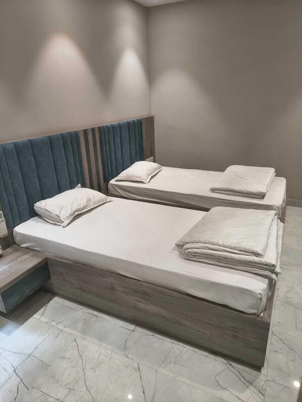 A hotel room with two beds, a wooden headboard, a marble floor, and a nightstand. - Hotel Sun-Om (Raipur)