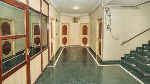 A hallway with a marble floor, wooden doors, and a staircase with green steps. - Hotel Sun-Om (Raipur)