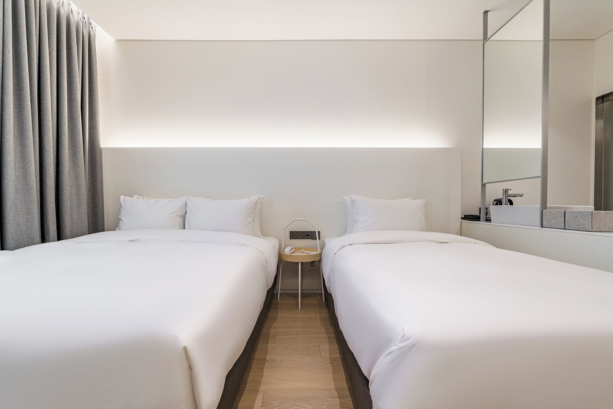 Habitació d'hotel amb dos llits, una petita taula de nit amb un telèfon i un mirall a la paret.