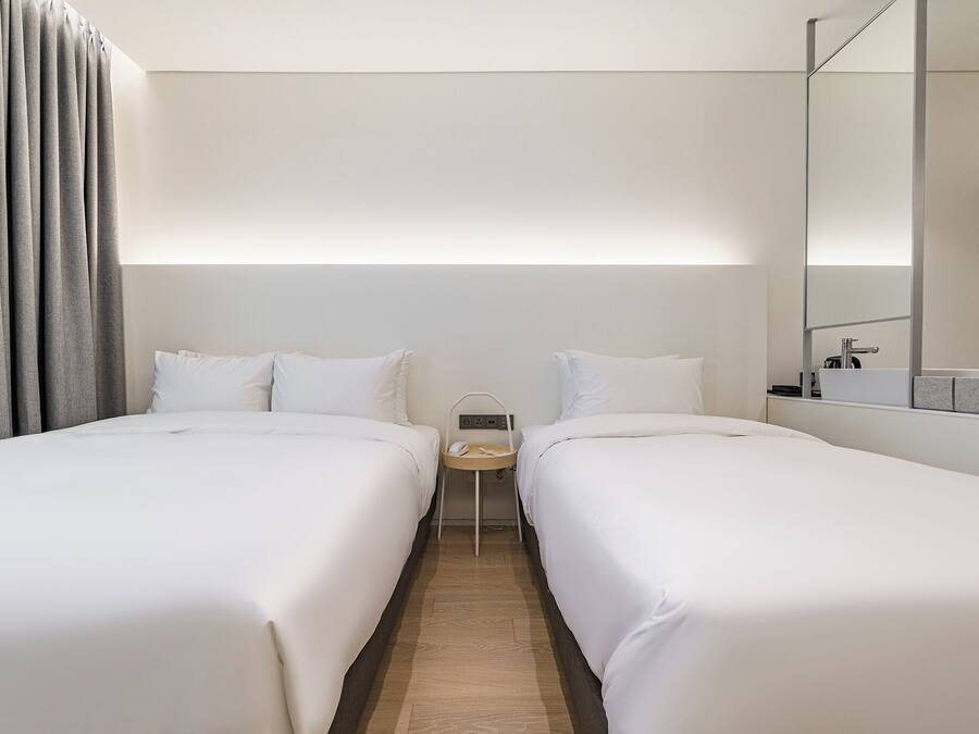 Habitació d'hotel amb dos llits, una petita taula de nit amb un telèfon i un mirall a la paret.