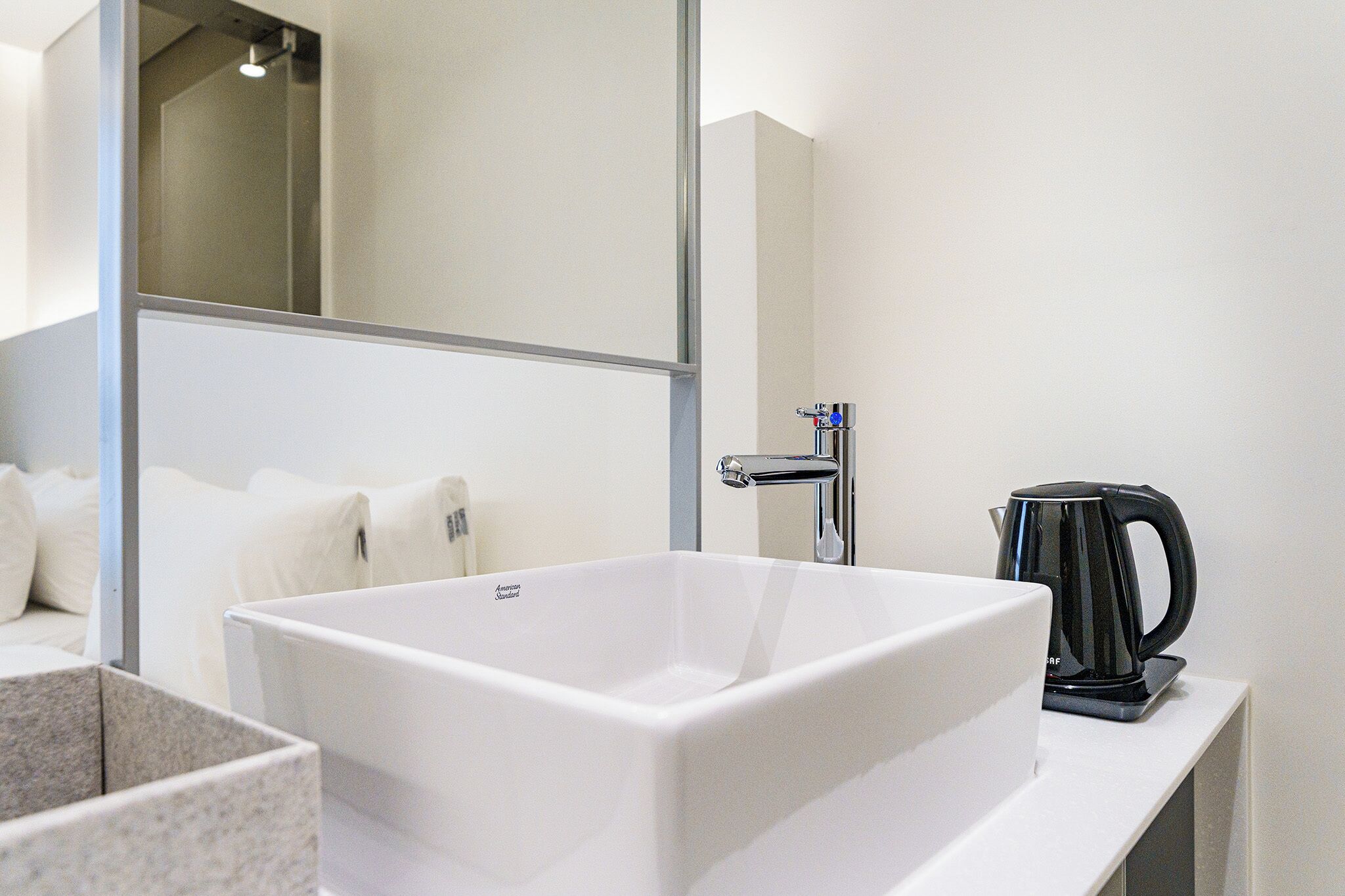 A modern bathroom with a white sink, a mirror, and a black coffee maker on the counter.