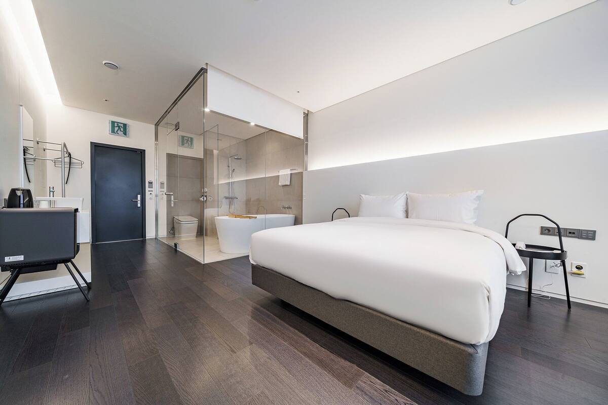 Ein modernes Hotelzimmer mit einem großen Bett, einem Schreibtisch, einer Dusche und einer Glasabtrennung.