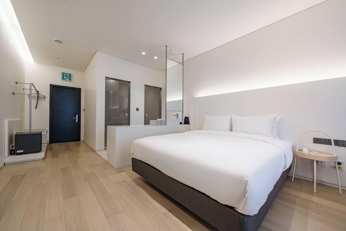 Ein modernes Hotelzimmer mit einem großen Bett, einem Nachttisch, einem Spiegel und einer kleinen Sitzecke.