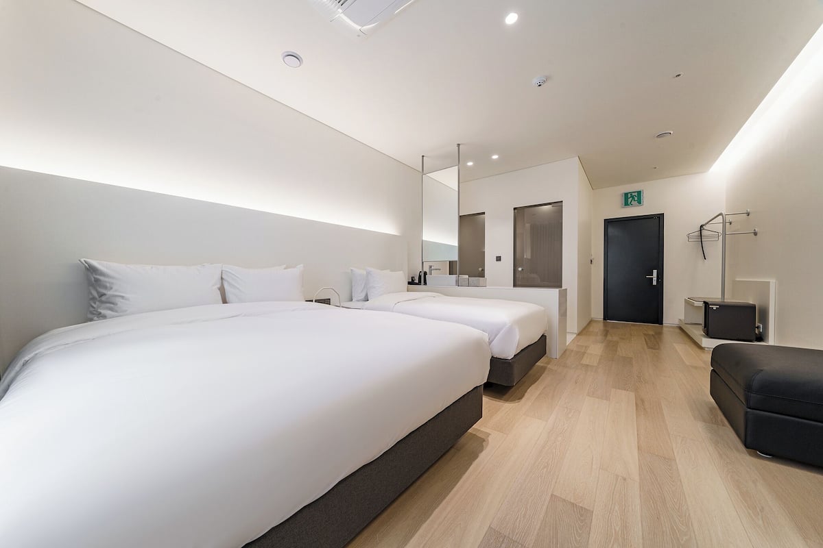 Ein modernes Hotelzimmer mit zwei Betten, einer Sitzecke und einer Tür zu einem Badezimmer.