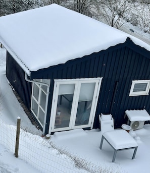 Um edifício coberto de neve com uma grande porta de correr de vidro, uma estrutura menor anexa e um quintal cercado.