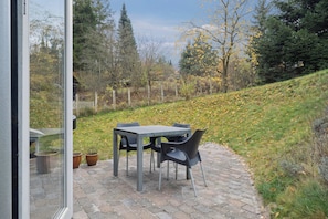 Une terrasse extérieure avec une table et des chaises, entourée d’une pelouse et d’arbres.