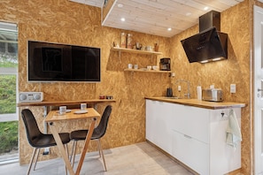 A modern kitchen with wooden walls, a built-in stove, and a dining area with a table and chairs.