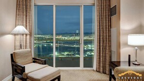 A hotel room with a large sliding glass door, a chair, a table, and a lamp. - MGM Signature-33-714 Penthouse 1BR w/ Balcony View (Las Vegas)