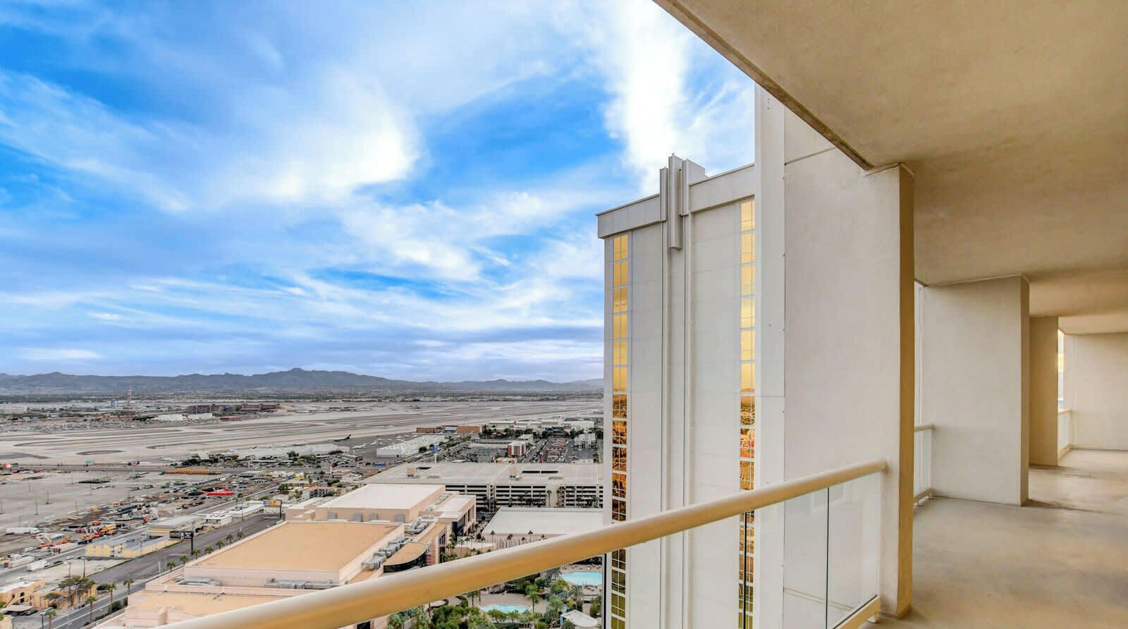 A high-rise hotel room with a balcony overlooking a cityscape and a desert landscape.