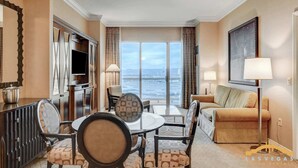 A hotel room with a dining area, a sofa, a TV, and a large window offering a view of the sea. - MGM Signature-33-714 Penthouse 1BR w/ Balcony View (Las Vegas)